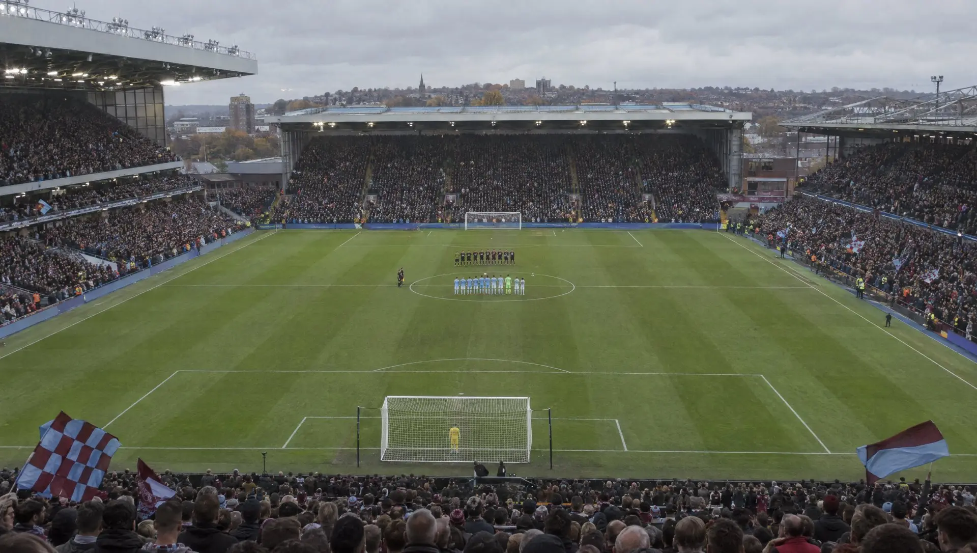 A full English football stadium on matchday with fans in the stands and players on the pitch