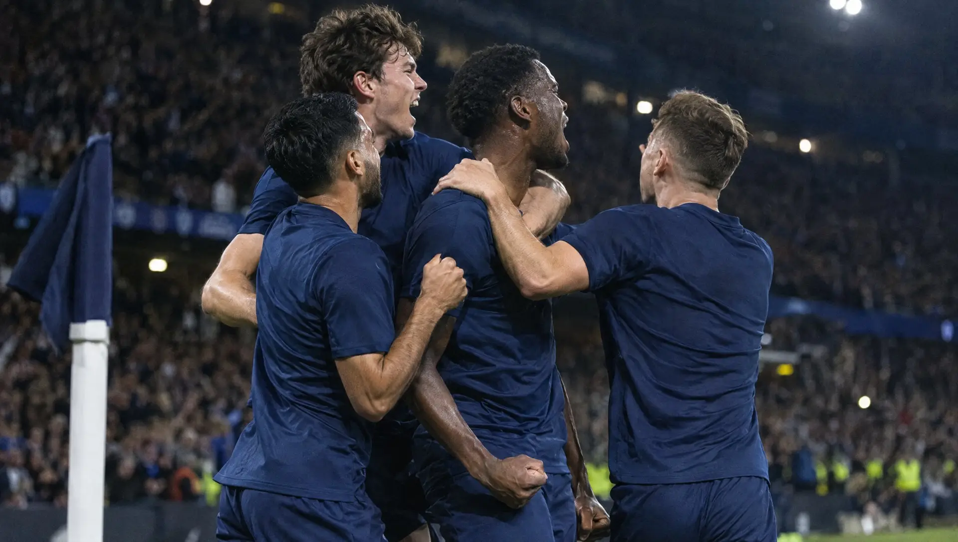 Footballers celebrating together on the pitch under floodlights after a big European win